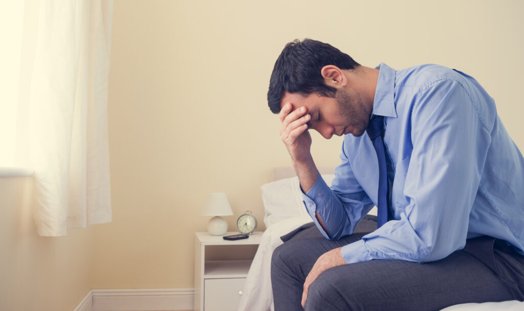 man distressed sitting on a bed with hand on his head